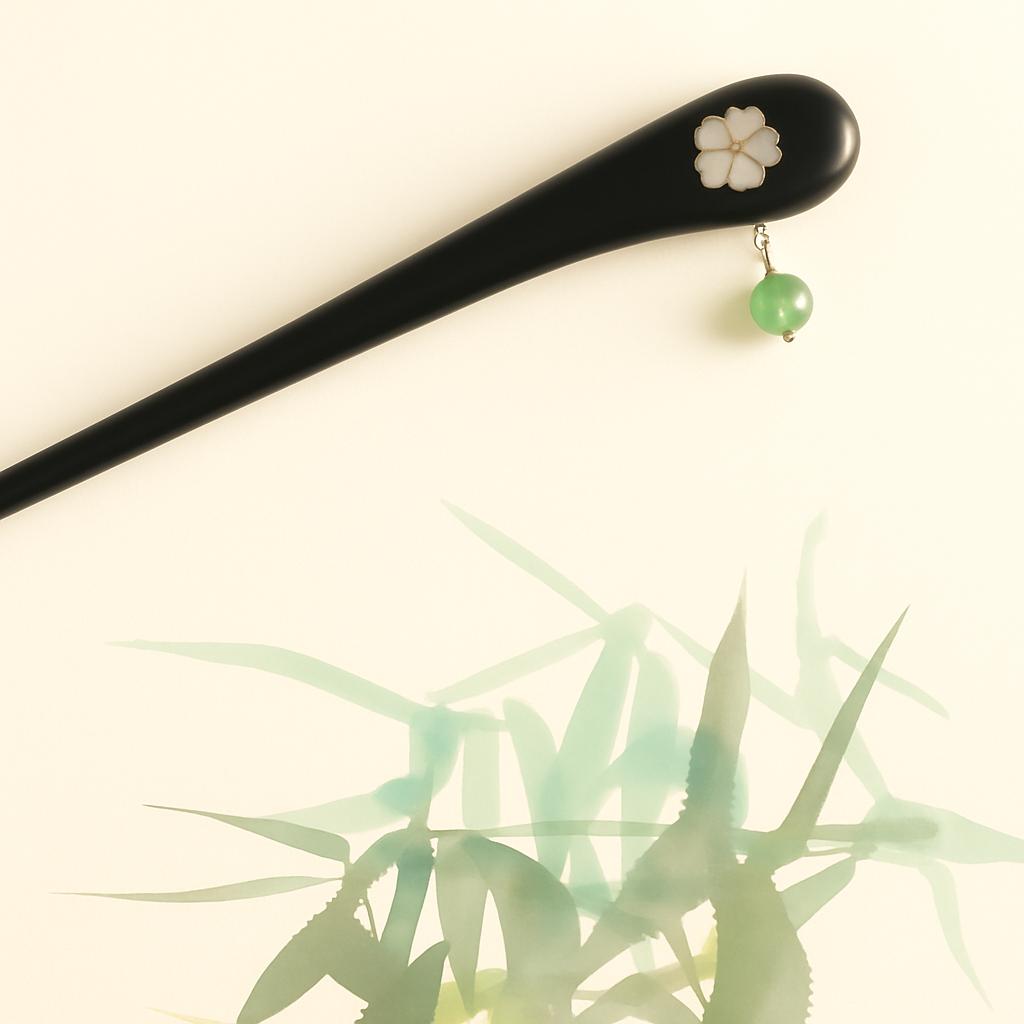 Black hairpin with floral design and green bead on a light background