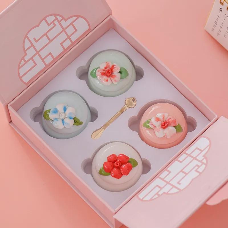 Four solid perfume balms with floral designs in a pink gift box