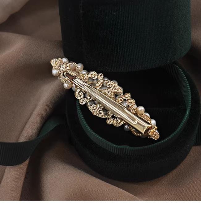 Gold hair barrette with pearls on a green velvet cushion