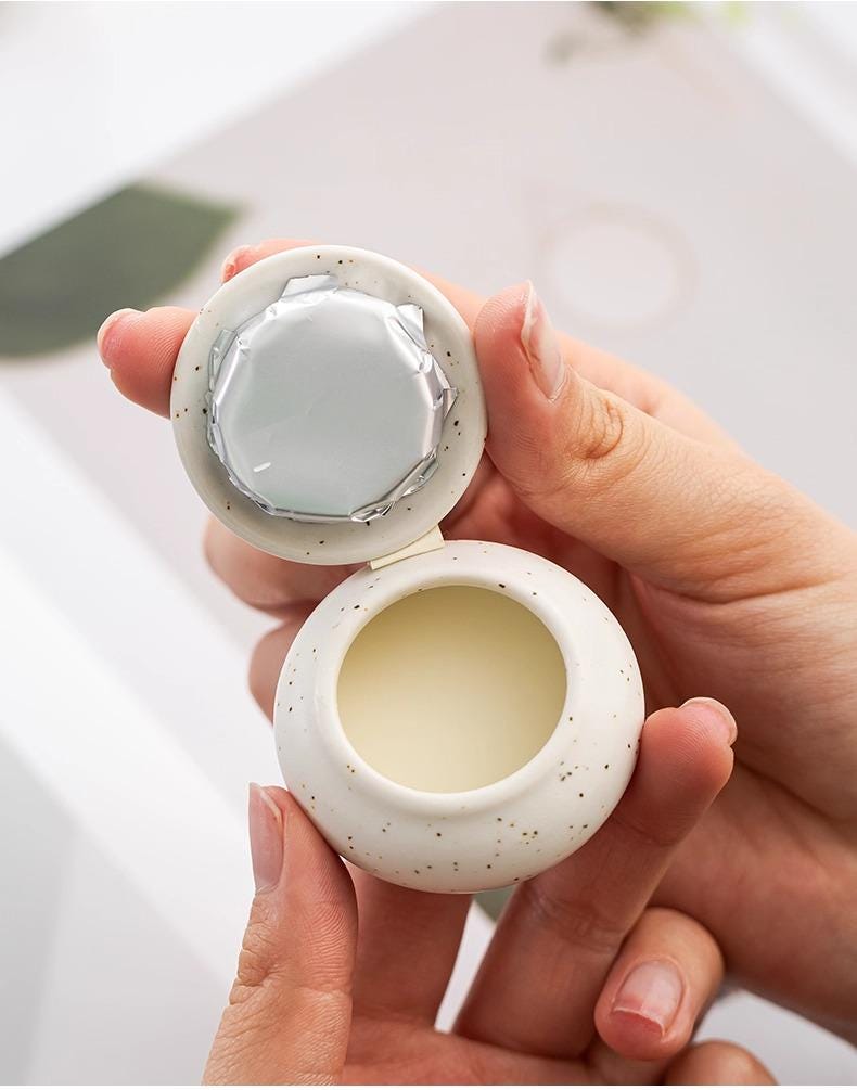 Hand holding a solid perfume (balm) with a lid.