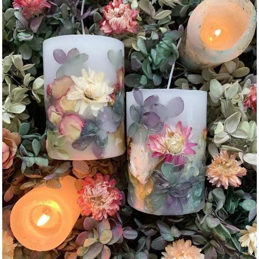 Decorative candles with floral designs on a bed of flowers and leaves.