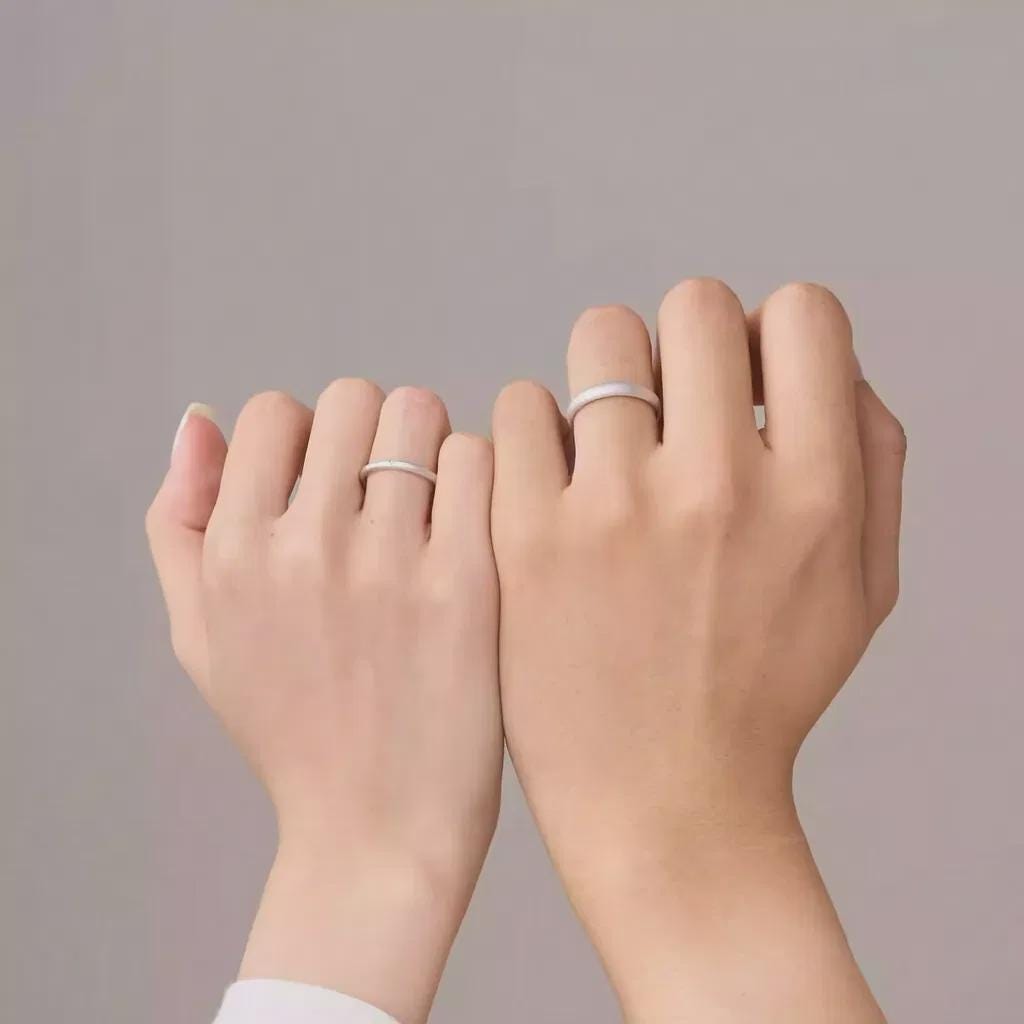 Two hands wearing silver rings on a plain background