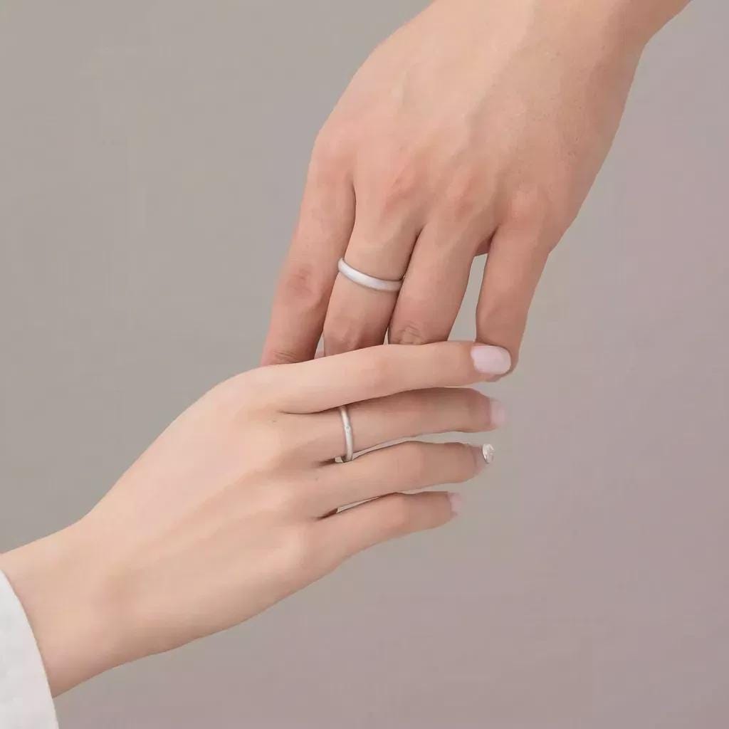 Two hands with silver rings on a plain background