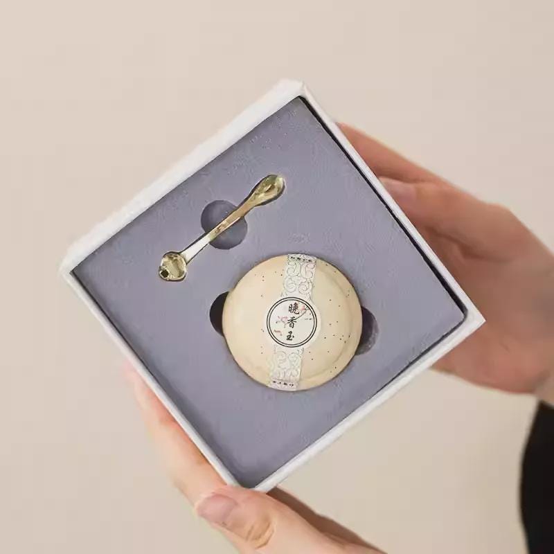 Balm with a spoon and round base in a box held by a hand.