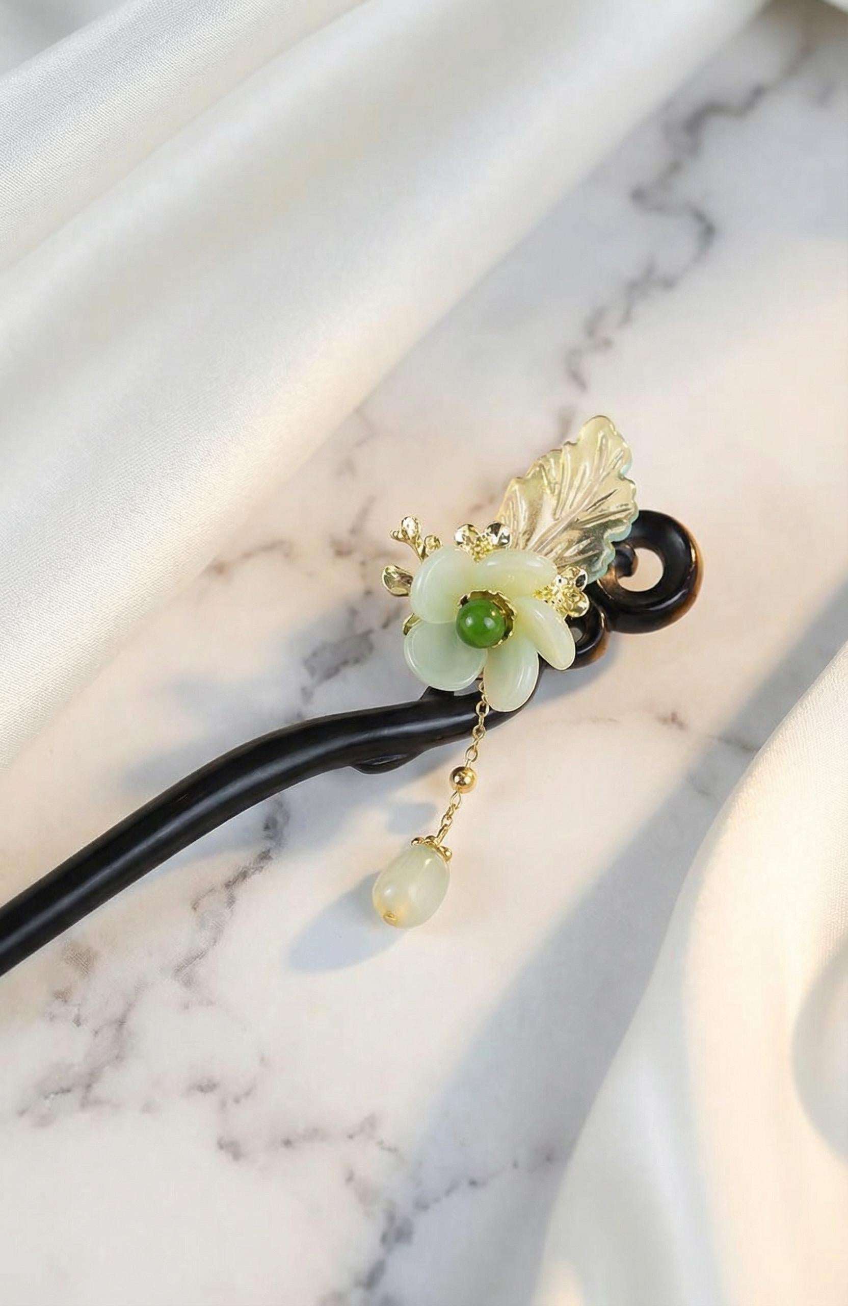 Decorative hairpin with green flower and gold accents on a marble background