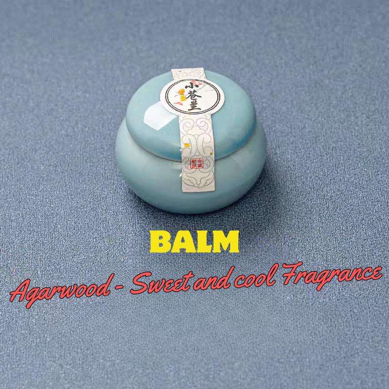 Blue balm container with a label on a gray background, featuring text about agarwood fragrance.