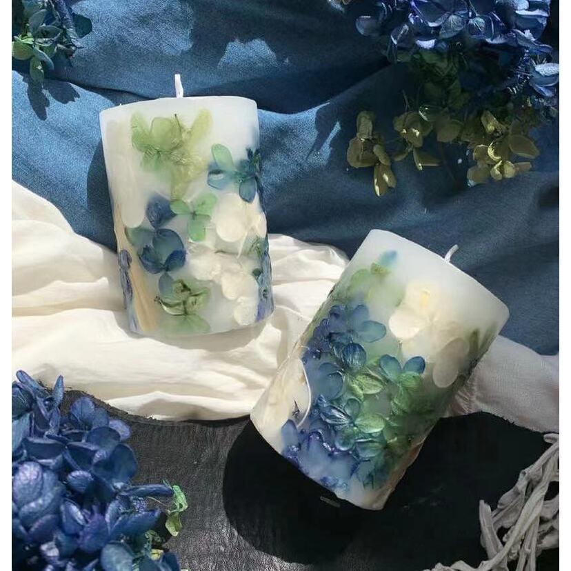 Decorative candles with floral designs on a textured surface with flowers around.