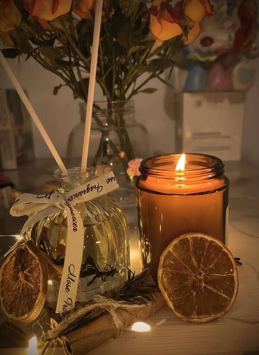 Candle in a jar with dried oranges and a decorative bottle on a table.