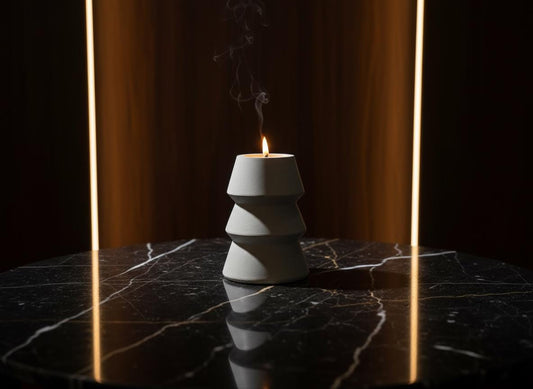 Cylindrical concrete candle holder with a lit candle on a dark marble surface.