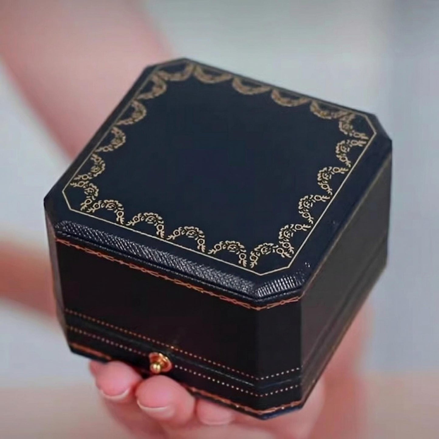 Decorative black jewelry box with gold accents held by a hand against a neutral background