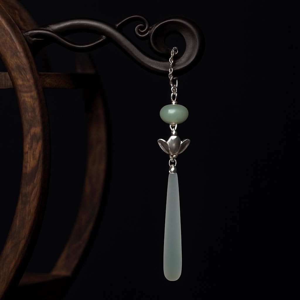 Decorative earring with green stone and silver chain on a dark background