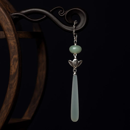 Decorative earring with green stone and silver chain on a dark background