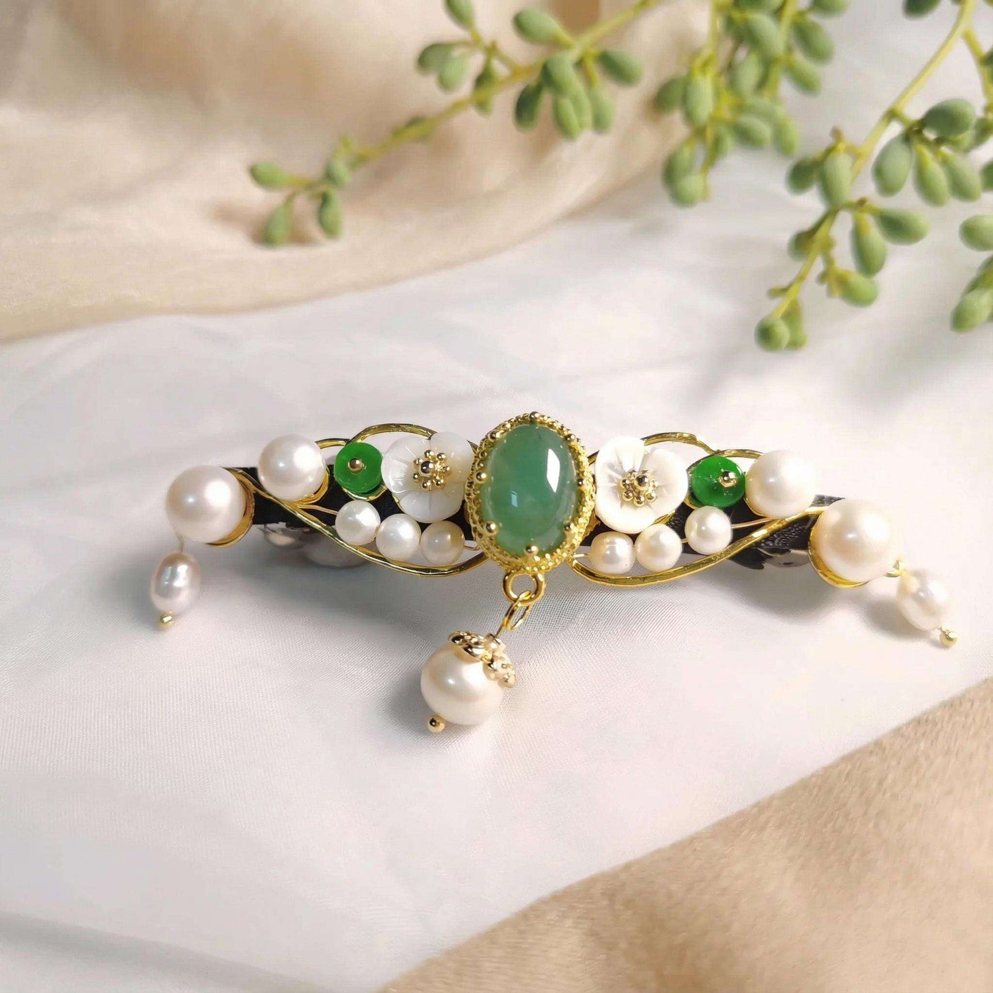 Decorative hair accessory with pearls and green stones on a neutral background