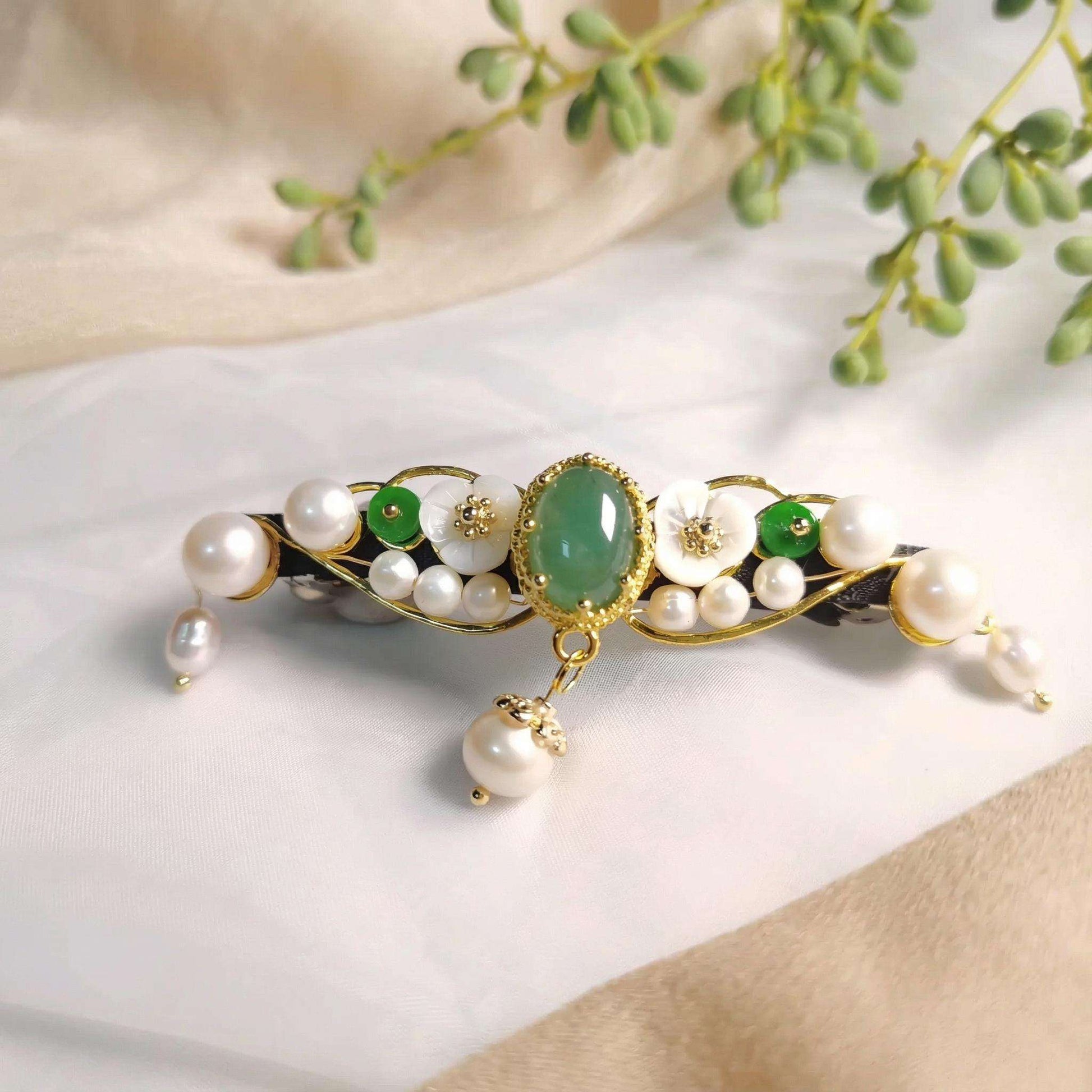 Decorative hair accessory with pearls and green stones on a neutral background