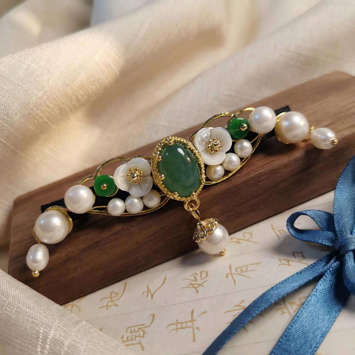 Decorative hair accessory with pearls and green stones on a wooden stand
