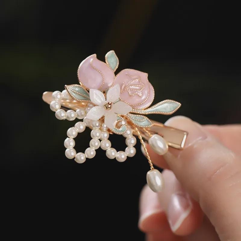 Decorative hair clip with floral design and pearls held by a hand against a dark background
