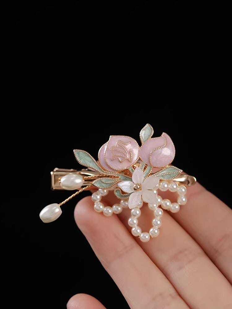 Decorative hair clip with floral design held by a hand against a black background