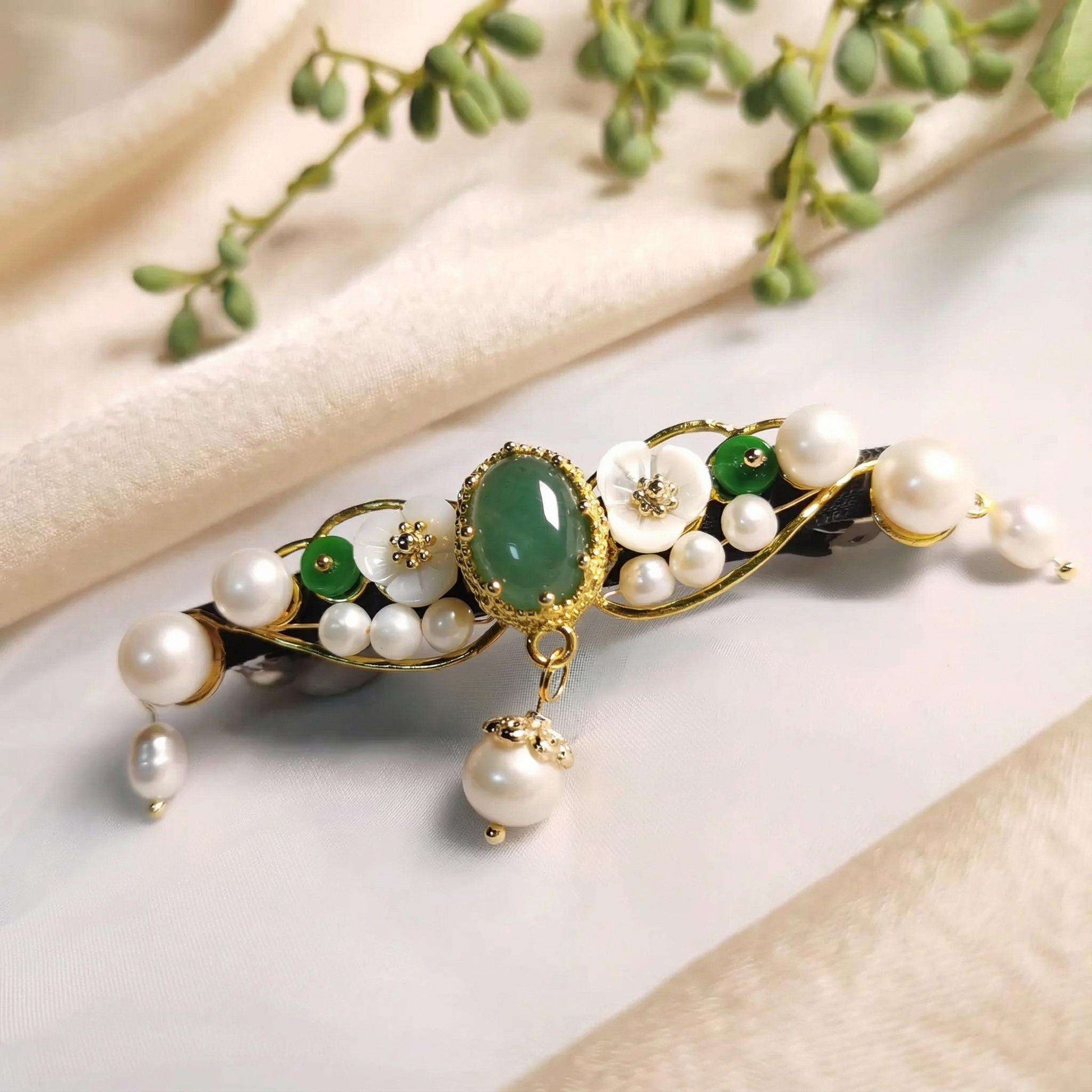 Decorative hair clip with pearls and green stone on a light background