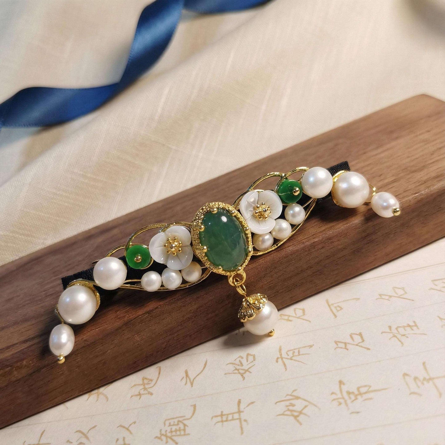 Decorative hair clip with pearls and green stones on a wooden surface
