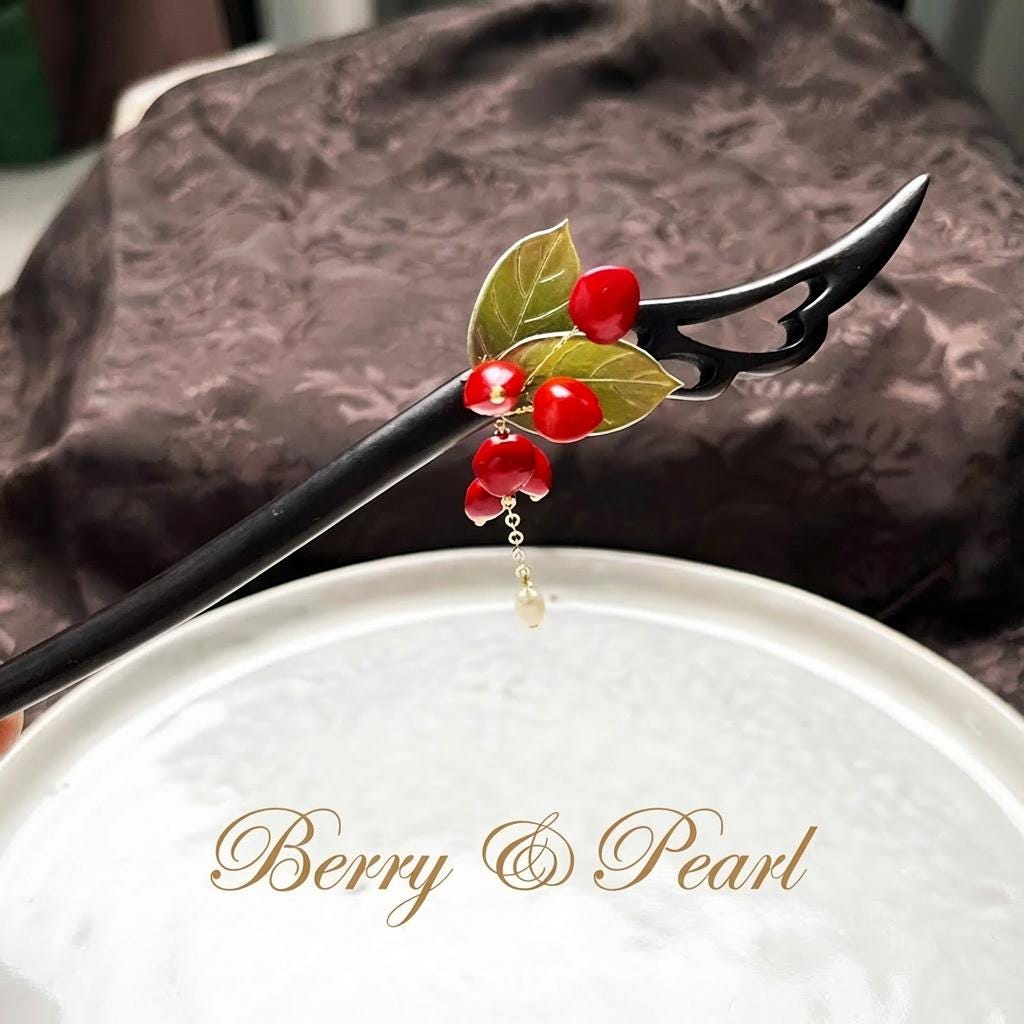 Decorative hairpin with red berries and green leaves on a white surface with 'Berry & Pearl' branding.