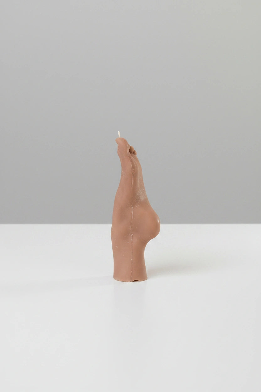 Brown ceramic candle holder shaped like a foot on a white surface with a gray background