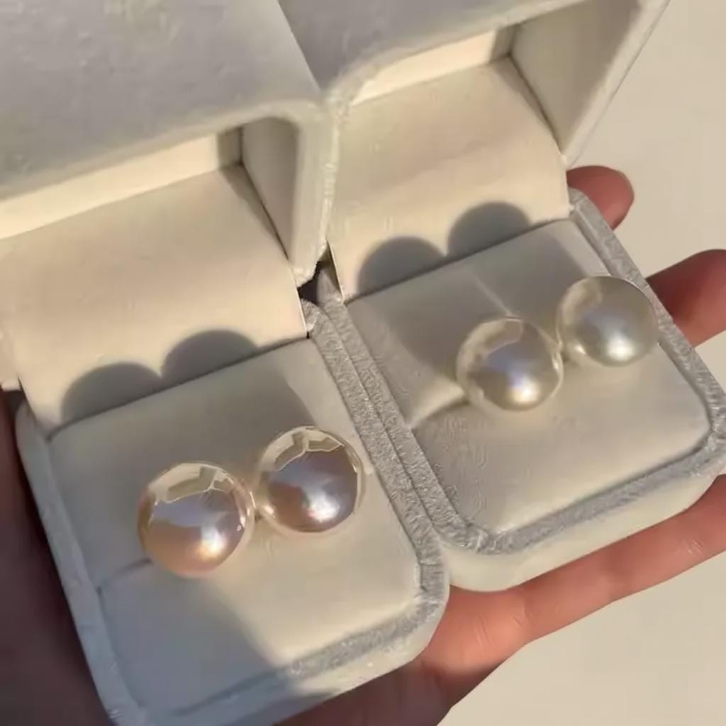 Gold earrings in a jewelry box held by a hand