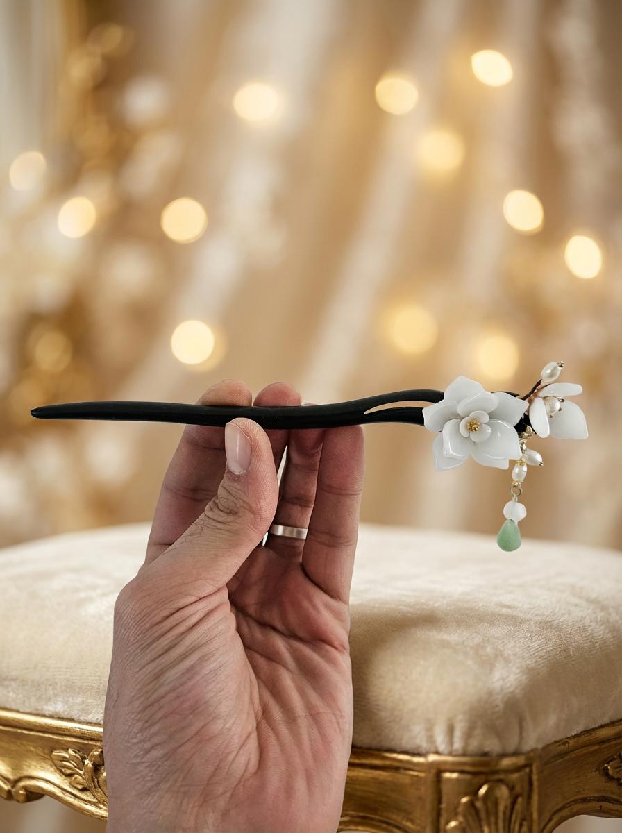 Hand holding a decorative hairpin with floral and pearl details against a blurred background