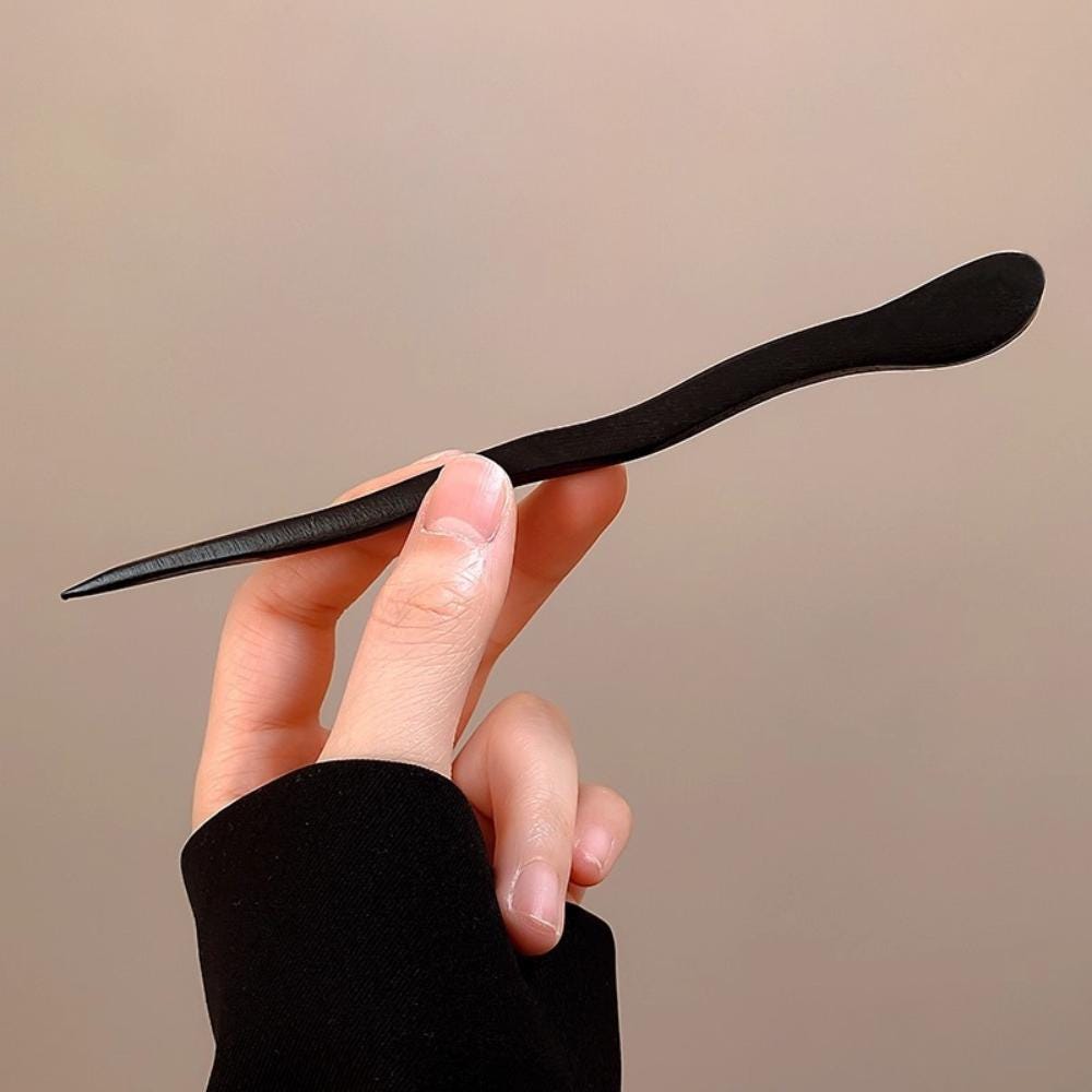 Hand holding a black hair straightener against a beige background