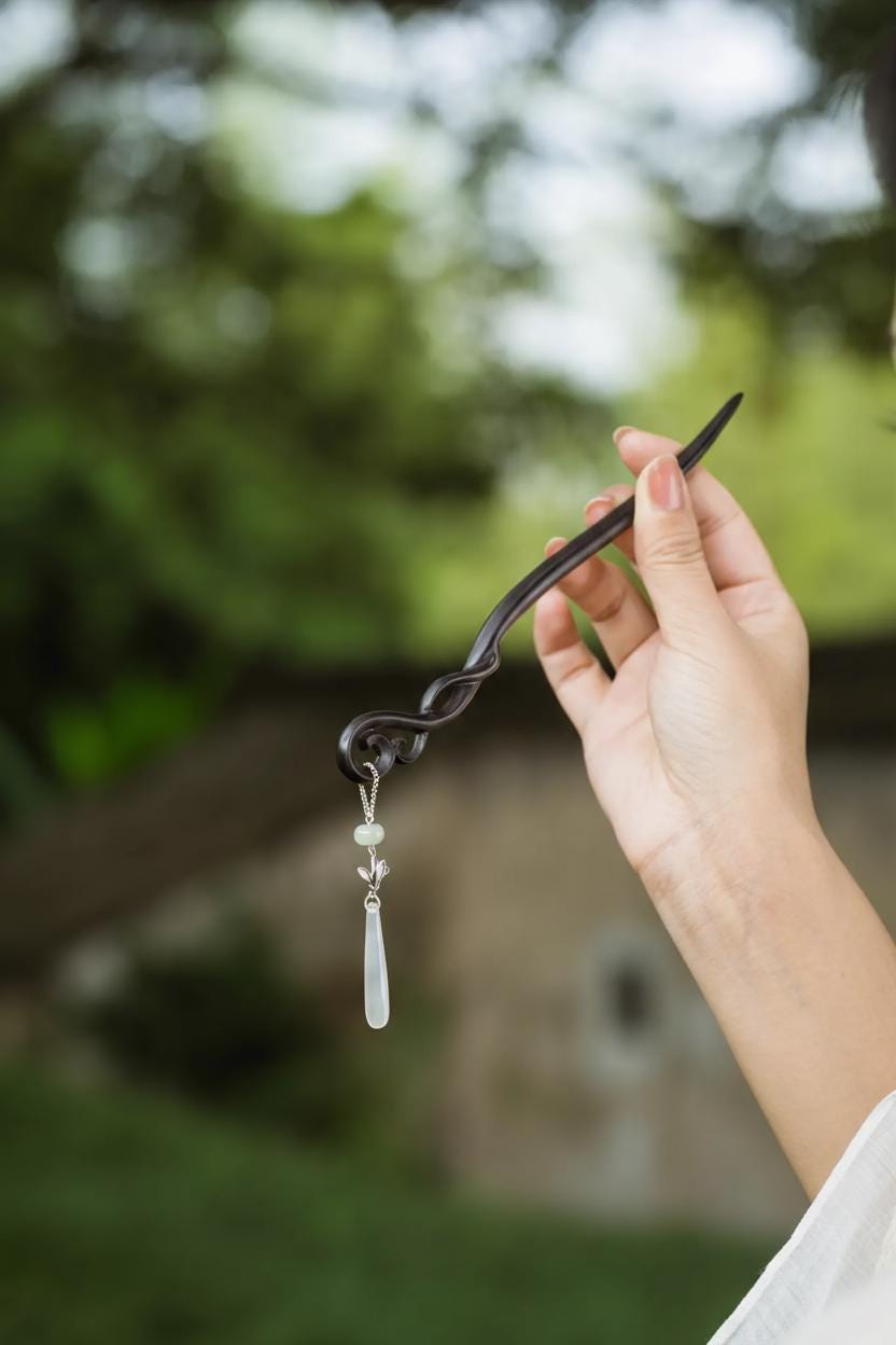 Hand holding a black hairpin with a white pendant against a blurred natural background