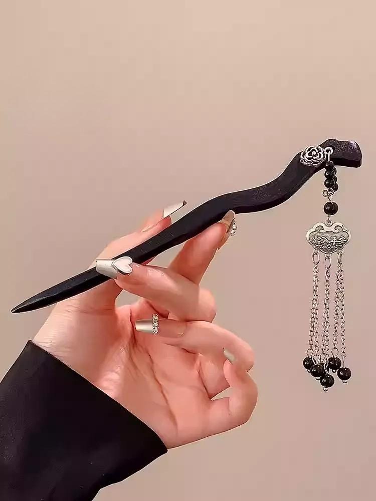Hand holding a decorative hairpin with intricate design against a beige background