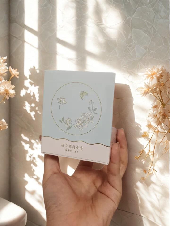 Hand holding a light blue box with floral design against a soft, sunlit background