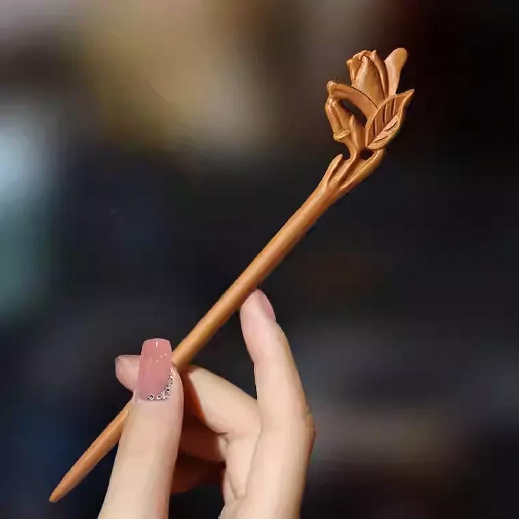 Hand holding a wooden hairpin with floral design against a blurred background