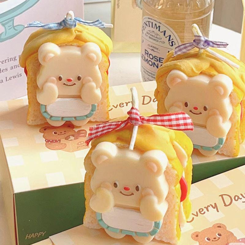 Three cute bear-shaped candles with yellow hair and blue ribbons on a table.