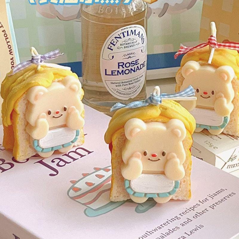 Two bear-shaped toast figurines with yellow hair and blue ribbons in front of a Fentimans Rose Lemonade bottle.