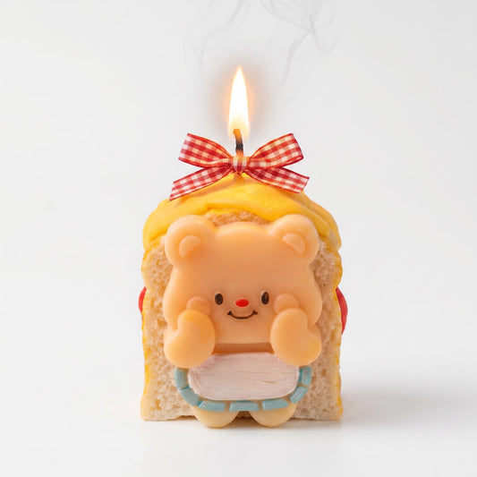 Candle shaped like a bear in a slice of bread with a bow on top, against a white background