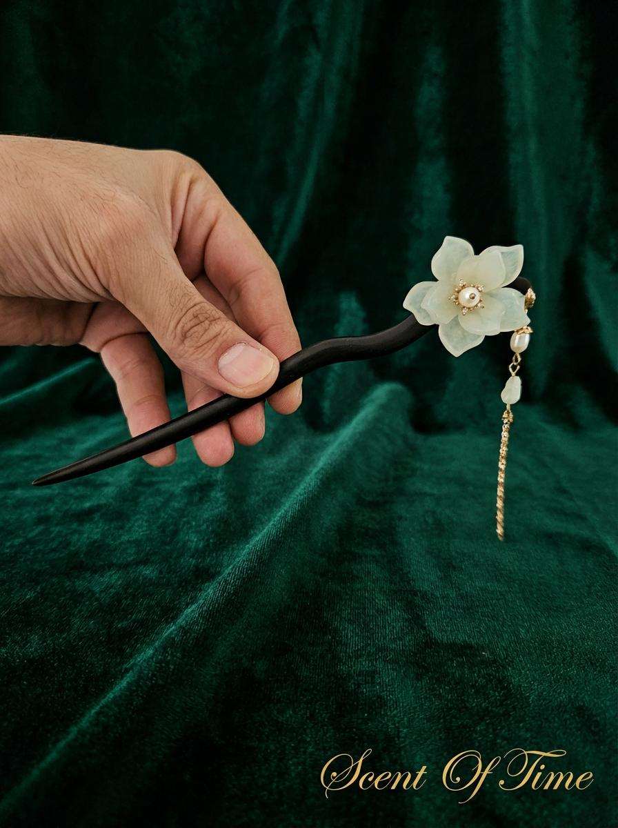 Hand holding a decorative hairpin with floral design against a dark green fabric background
