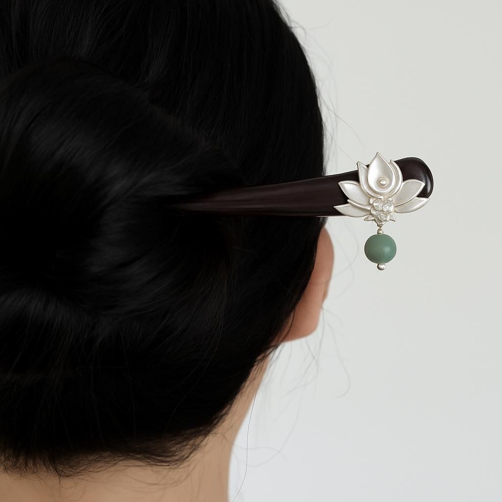 Hairpin with lotus design and green bead on black hair against a white background