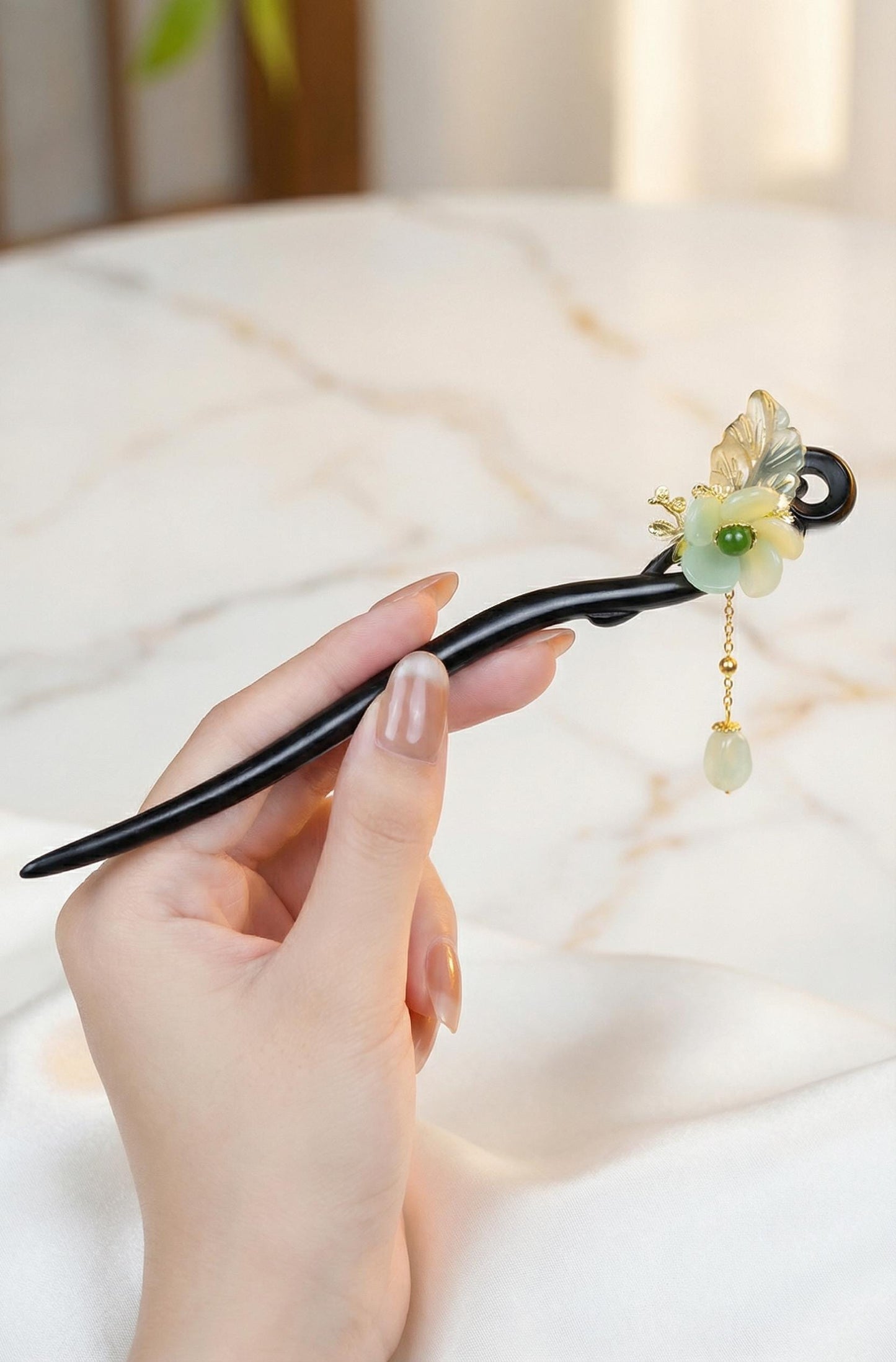Hand holding a decorative hair stick with floral design and beads on a soft background