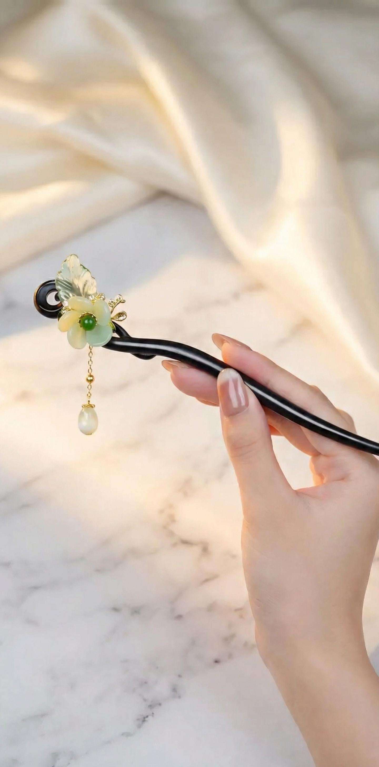 Hand holding a decorative hairpin with floral design on a marble surface