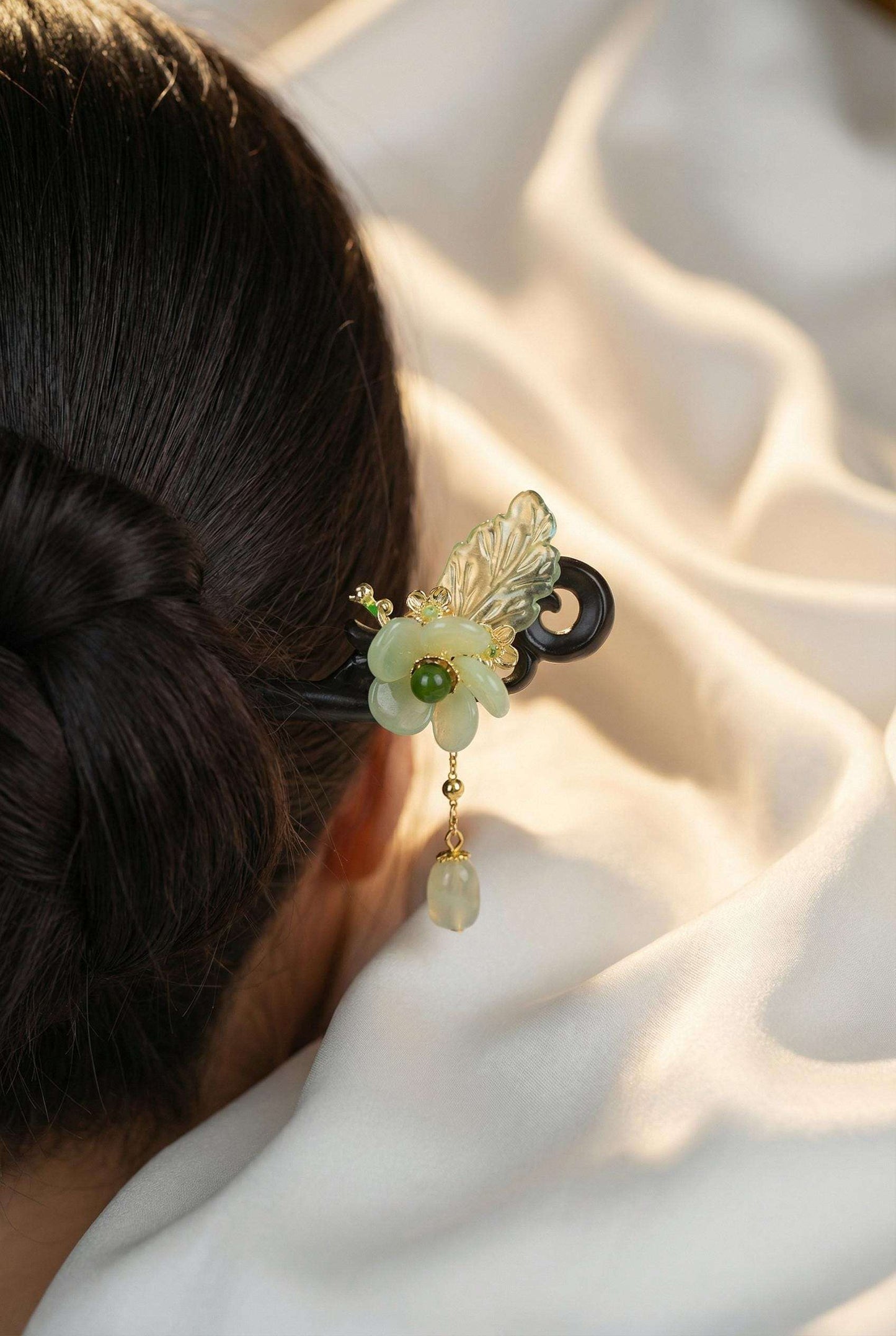 Decorative hair clip with floral design and green gemstone on a person's hair against a soft white background