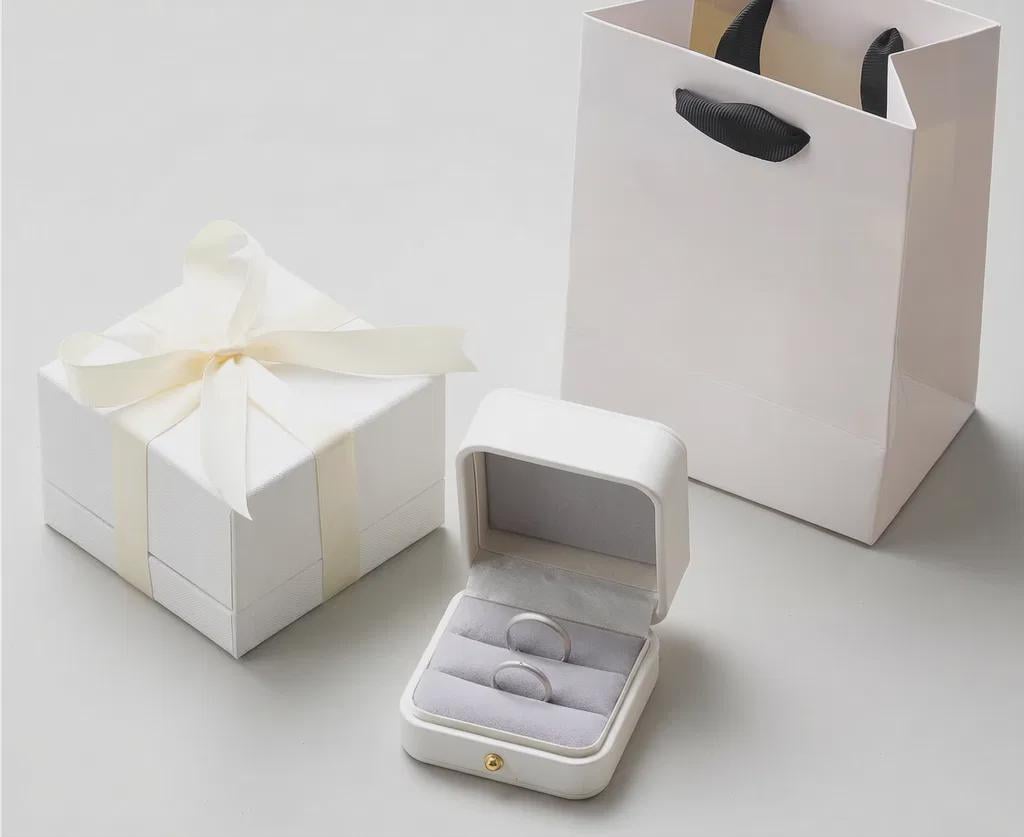 Jewelry box with ring inside, next to a white gift box and bag on a light gray background