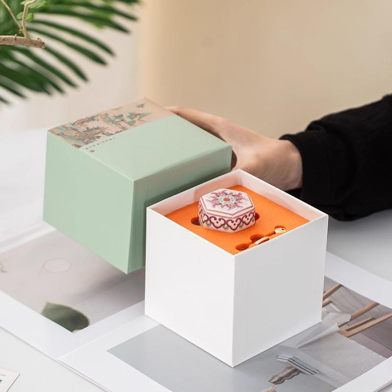 Person opening a white box with a green lid to reveal a Balm on an indoor setting.