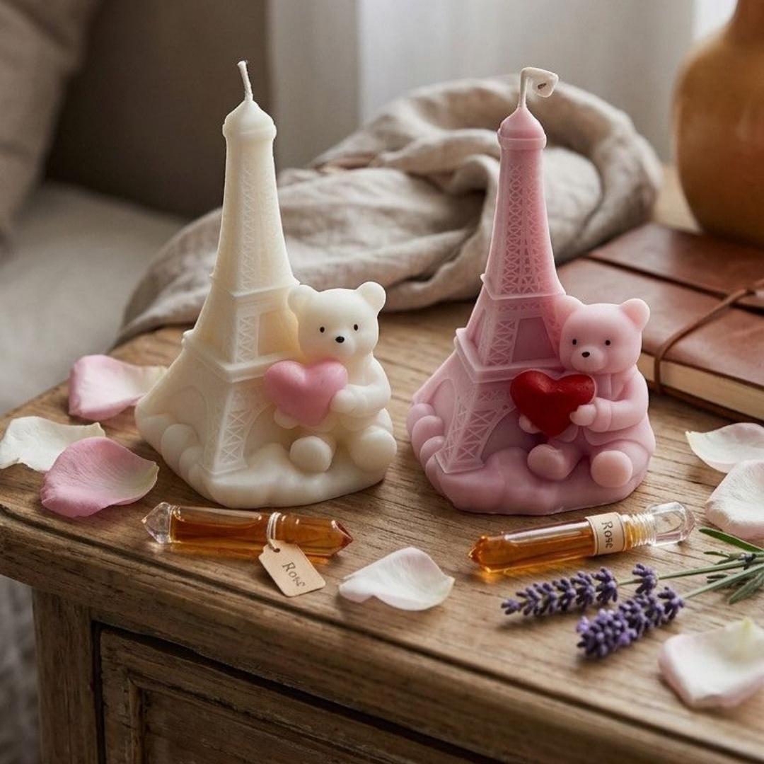 Two Paris Eiffel Tower Bear Candle on a wooden surface with flowers and a book.