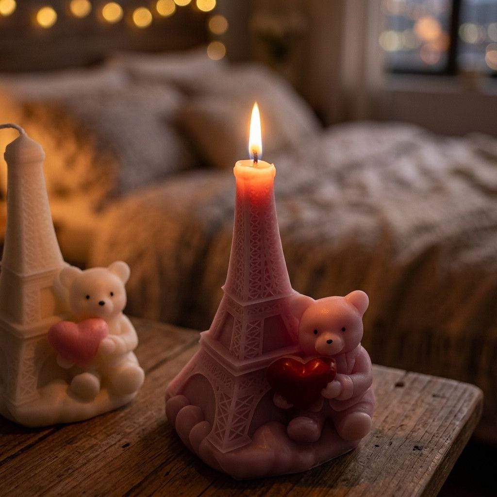 Pink Eiffel Tower candle with a lit flame on a wooden surface, surrounded by cozy decor.