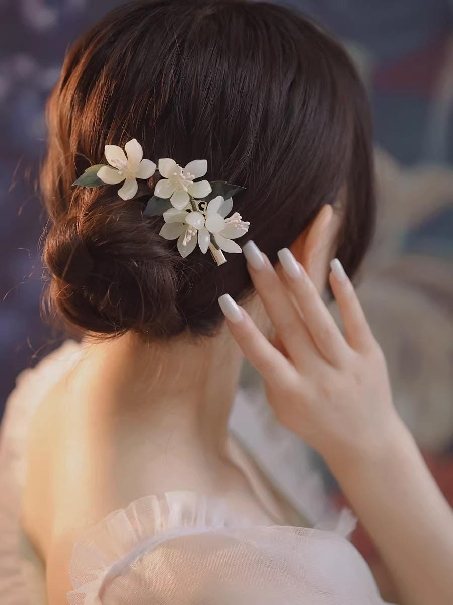 Person with floral hair accessory adjusting their hair against a blurred background