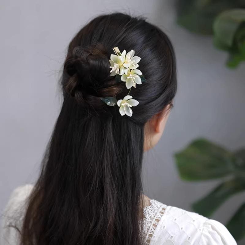 Person with long dark hair styled in a ponytail with floral hair accessories against a neutral background