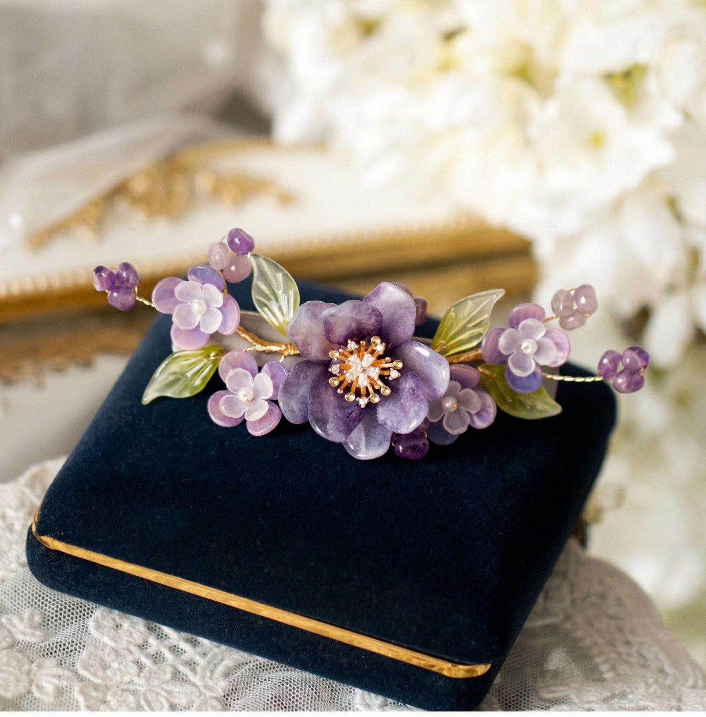 Purple Peony Ronghua Velvet Flower Hair Clip on a black velvet box with gold trim, against a blurred floral background.