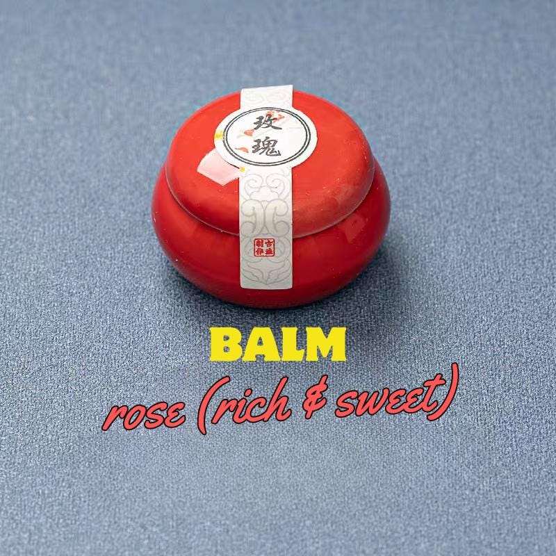 Red balm container with a label on a blue textured background, labeled 'Balm rose (rich & sweet)'.