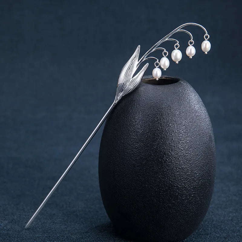 Silver hairpin with pearl-like beads on a black vase against a dark background