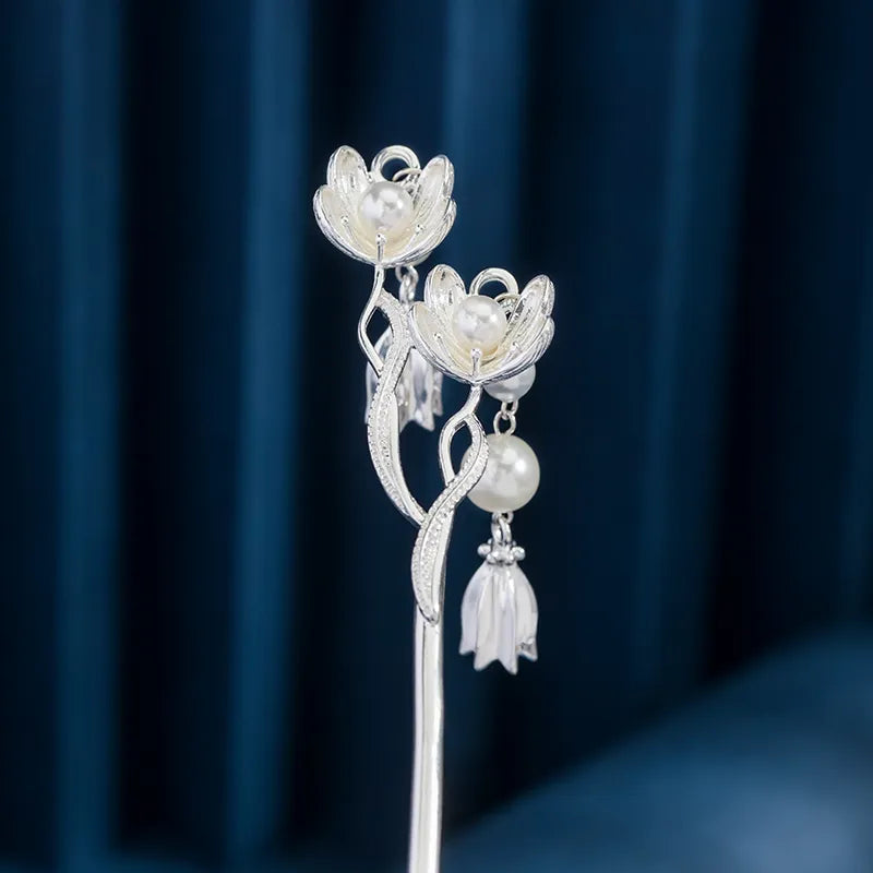 Silver hairpin with floral design and pearls against a dark blue background